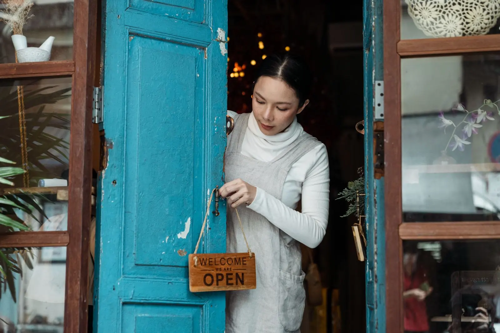 A shop owner hanging an open sign on a blue door